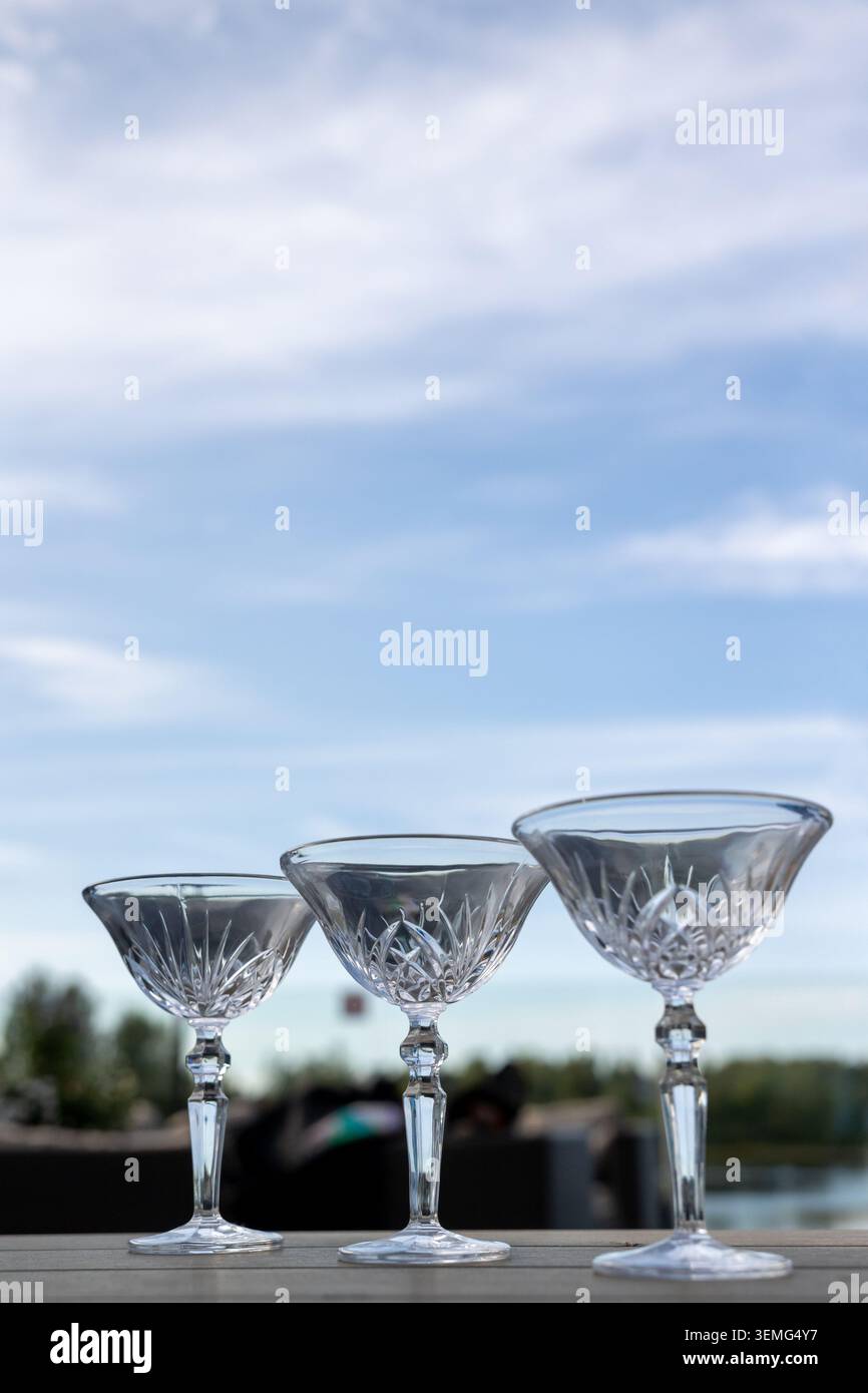 tre bicchieri da cocktail vuoti in fila sul tavolo all'aperto con cielo nuvoloso Foto Stock