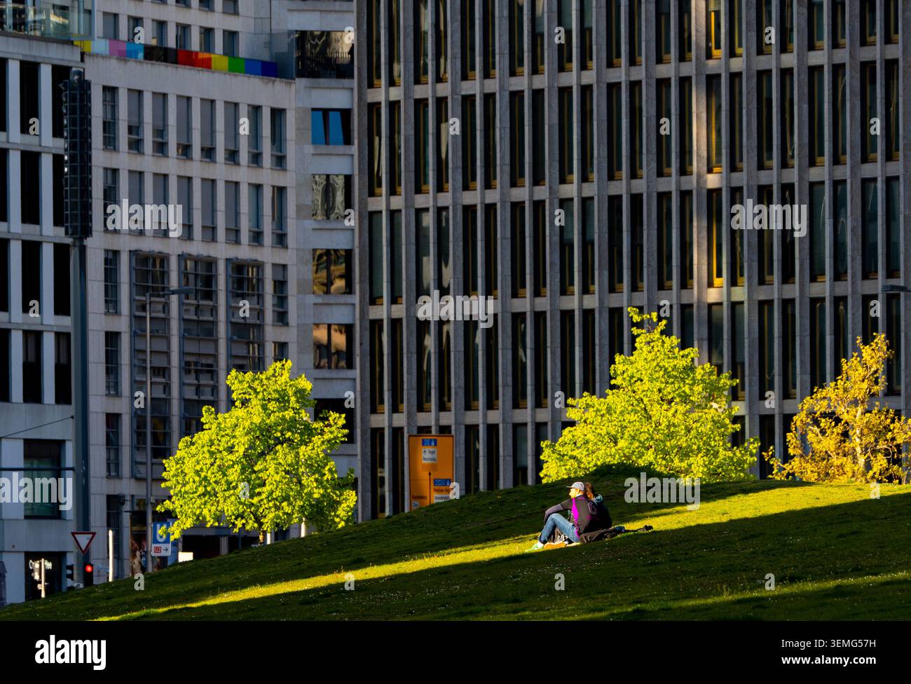 Coppia rilassante sul prato di Potsdamer Platz, Berlino, Germania, incorniciata da un'architettura contemporanea e da un fitto skyline urbano. Foto Stock