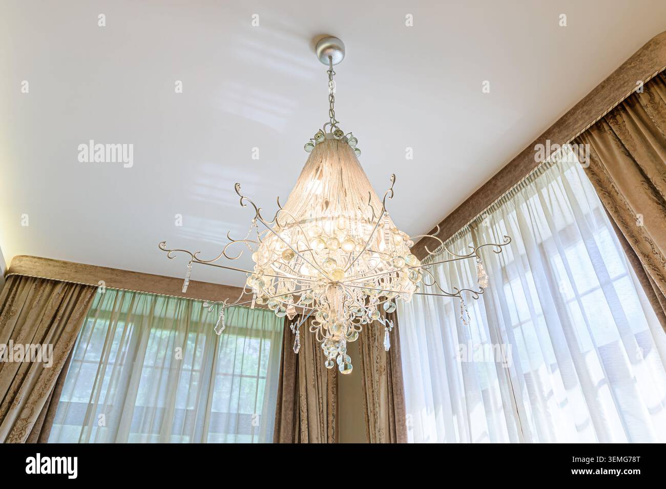 Elegante lampadario appeso al soffitto. Finestra con tende sullo sfondo. spazio arredato con gusto, possibilmente soggiorno o zona pranzo, con Foto Stock