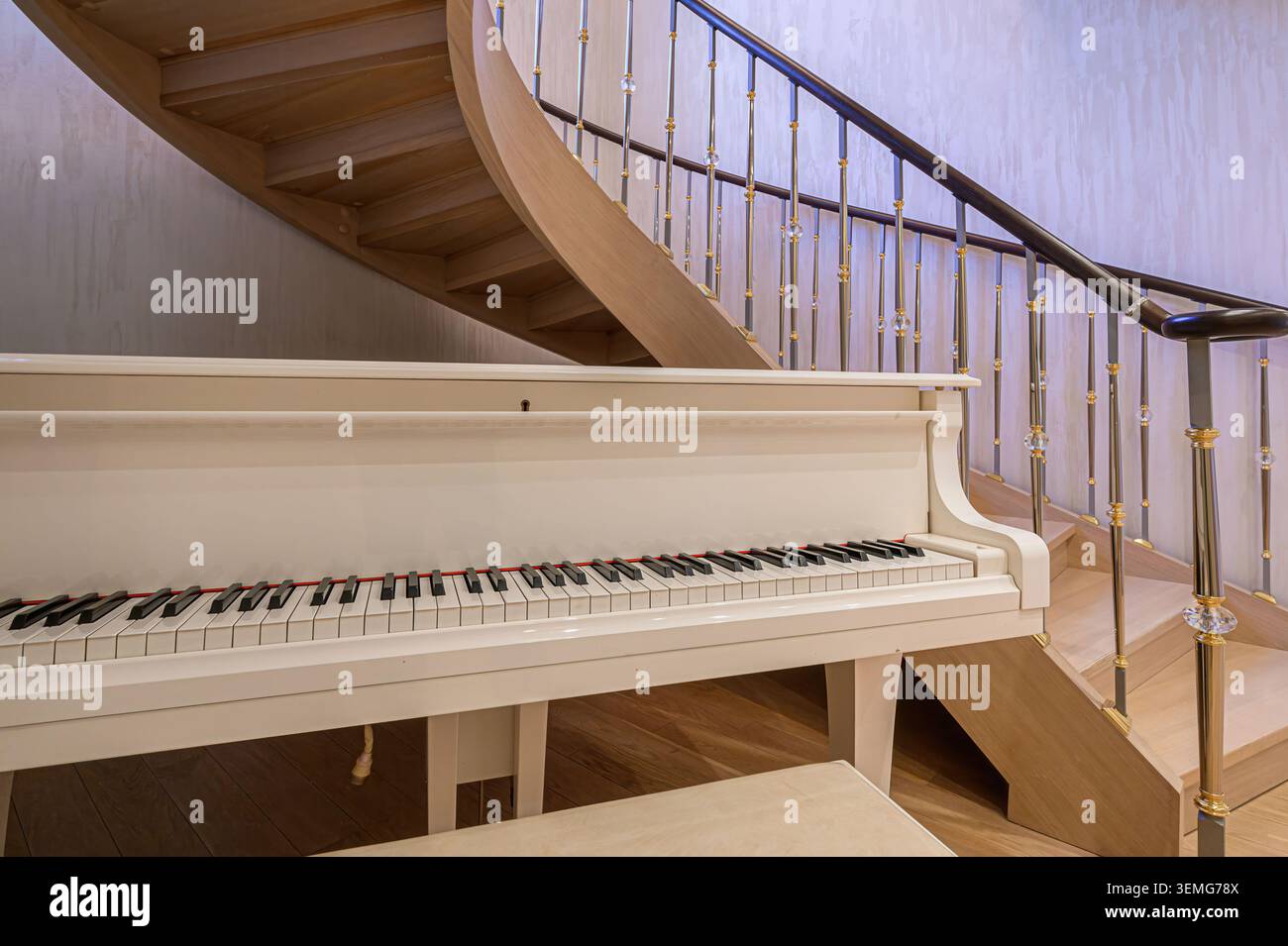 il pianoforte a coda bianco si erge vicino a una scala curva in legno chiaro con ringhiere decorative in metallo e cristallo in una stanza dai toni neutri. Foto Stock