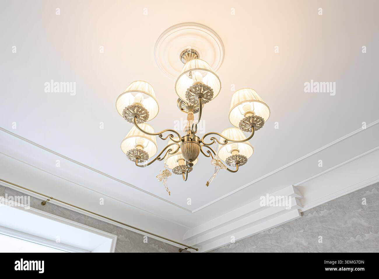 Elegante lampadario con sfumature crema, struttura in metallo ornato e pendenti in cristallo appesi a un soffitto bianco con modanatura Foto Stock
