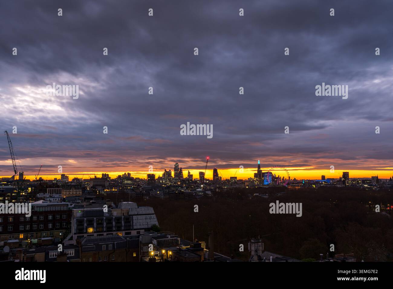 L'alba è mostruosa su Londra con pesanti nuvole scure e una striscia di luce dorata illuminata lungo l'orizzonte dietro lo skyline della città, Inghilterra, Regno Unito Foto Stock
