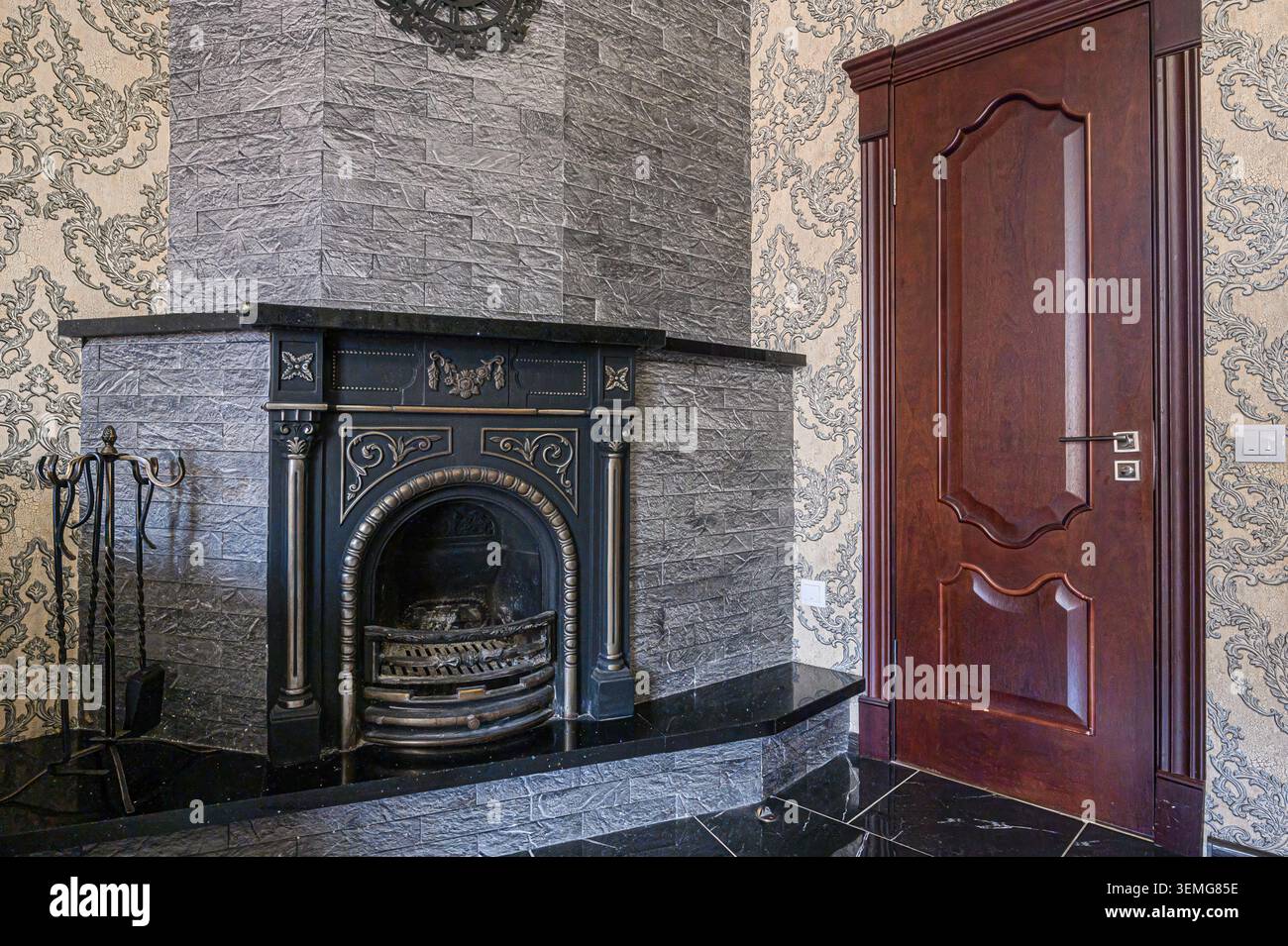 l'angolo della camera presenta un caminetto decorativo con cornice in pietra, accenti in marmo nero e una porta in legno scuro accanto alla carta da parati a motivi geometrici. Foto Stock