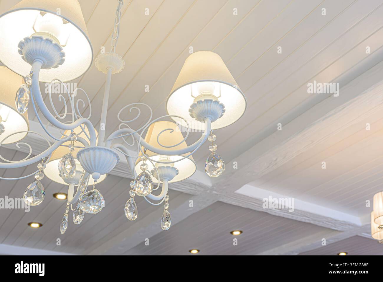 la foto ad angolo basso presenta un lampadario bianco decorato con pendenti in cristallo appesi alle braccia, appoggiati su un soffitto bianco a pavimento con li incassati Foto Stock