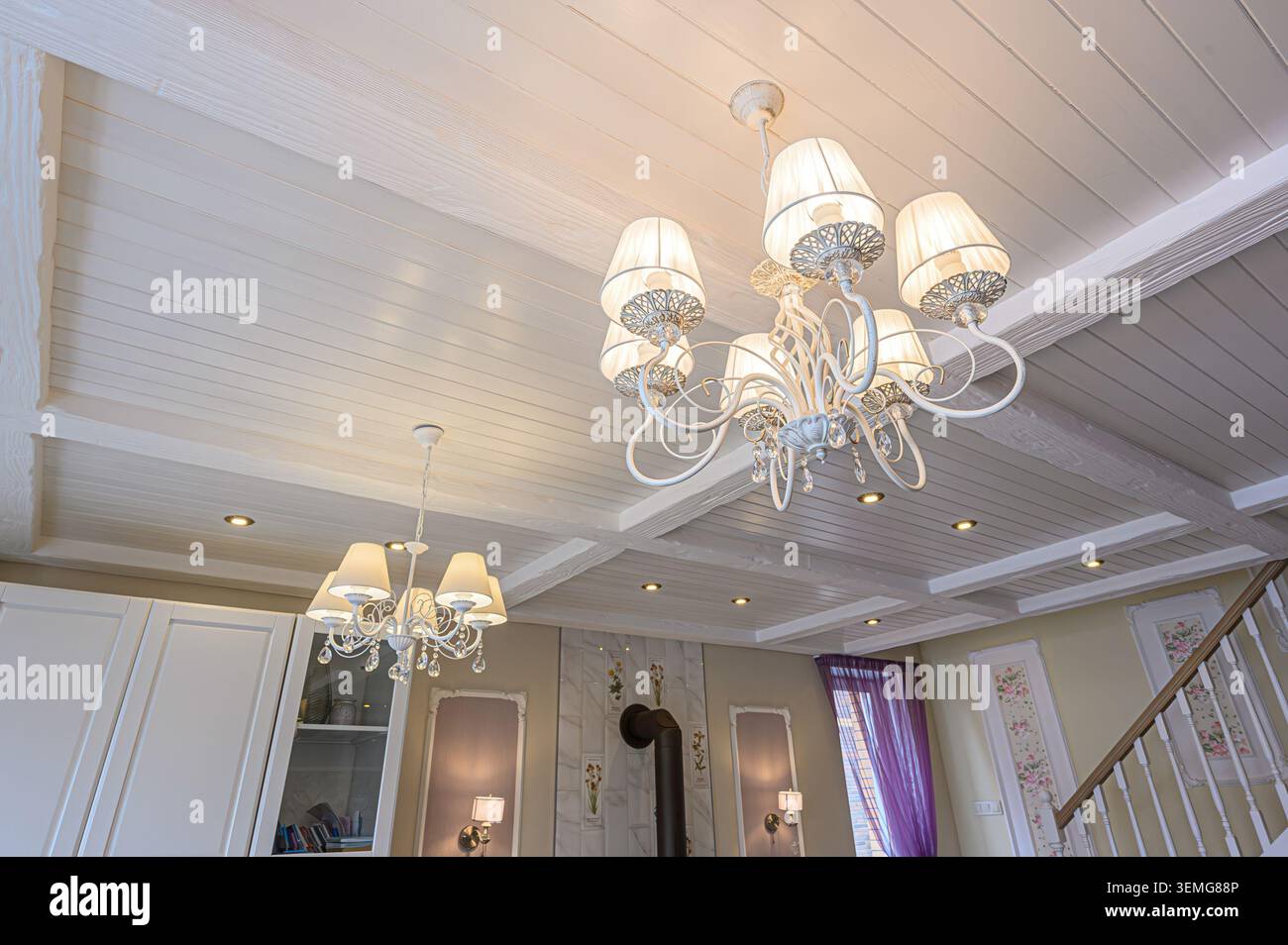 Camera elegante con soffitto a pannelli bianchi, lampadari e illuminazione a incasso. Presenta pareti decorative e dettagli delle scale. Foto Stock