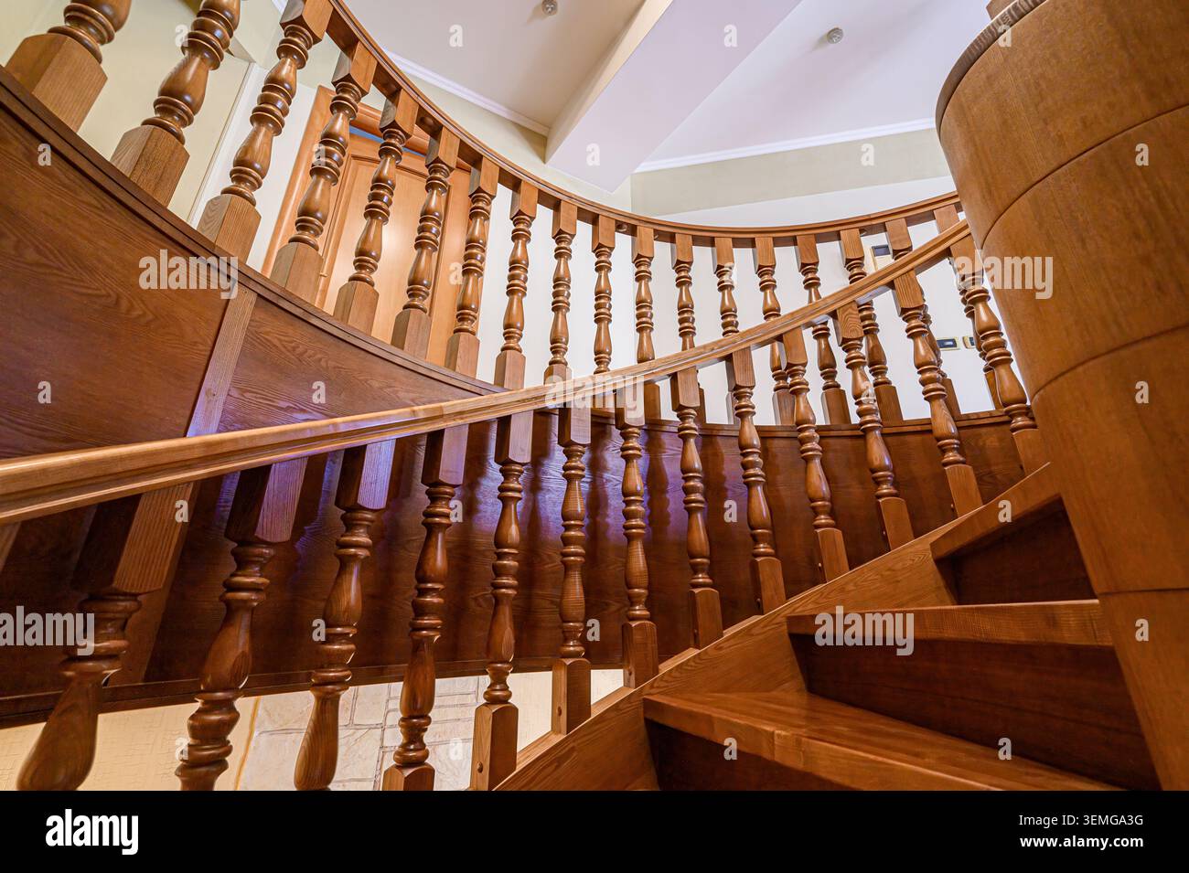 scala di legno con balaustre ornate. Le calde tonalità di legno e il design curvo creano un'atmosfera elegante e invitante. Foto Stock