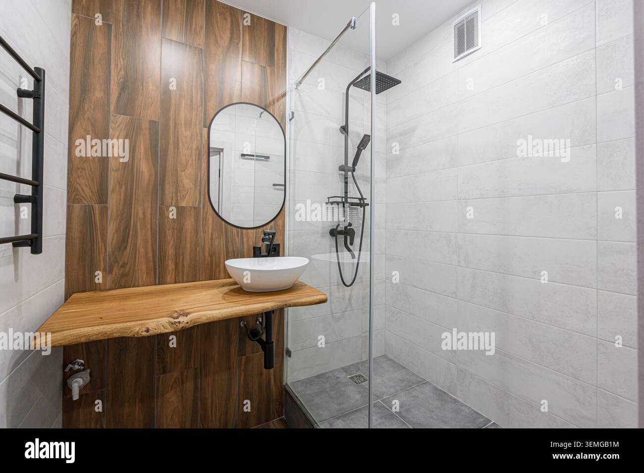 Bagno moderno con accenti in legno. Dispone di box doccia in vetro, specchio ovale e un esclusivo ripiano in legno con lavandino bianco Foto Stock