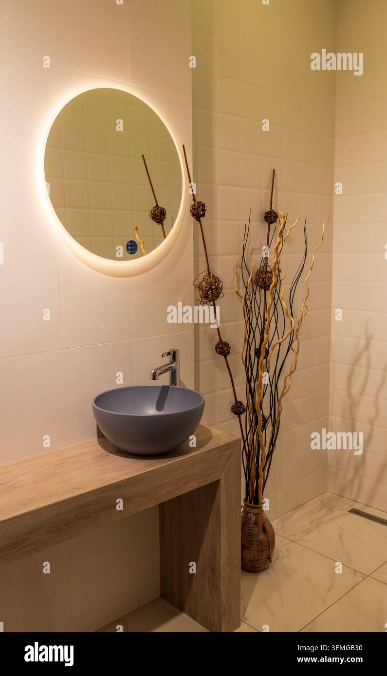 Bagno dal design contemporaneo con specchio retroilluminato circolare e console in legno Foto Stock