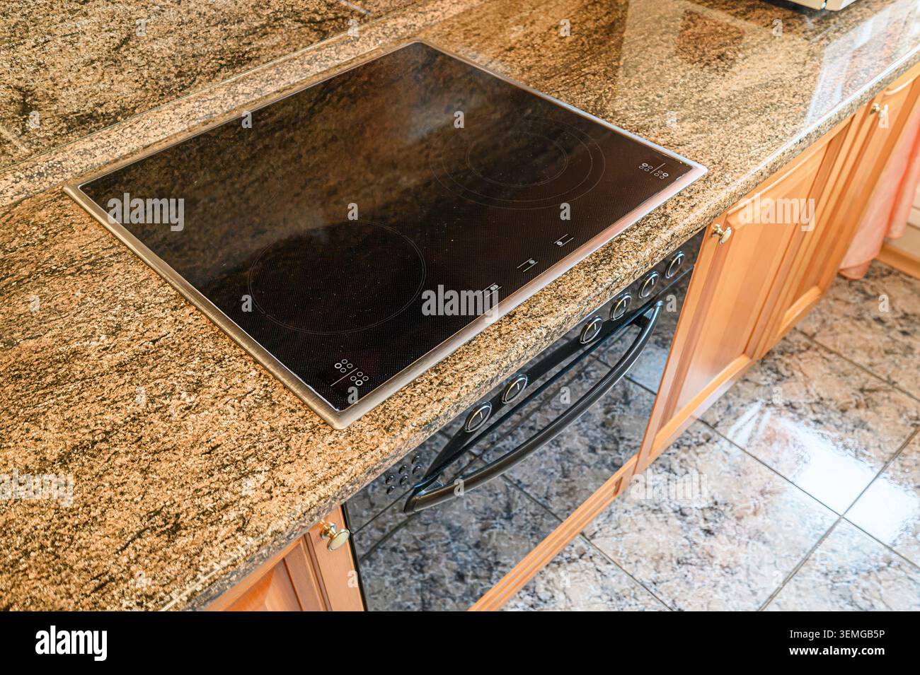 piano di lavoro della cucina con elegante piano cottura nero, superficie in granito e armadi in legno sotto un forno. Il piano di appoggio ha una superficie in granito e legno chiaro Foto Stock