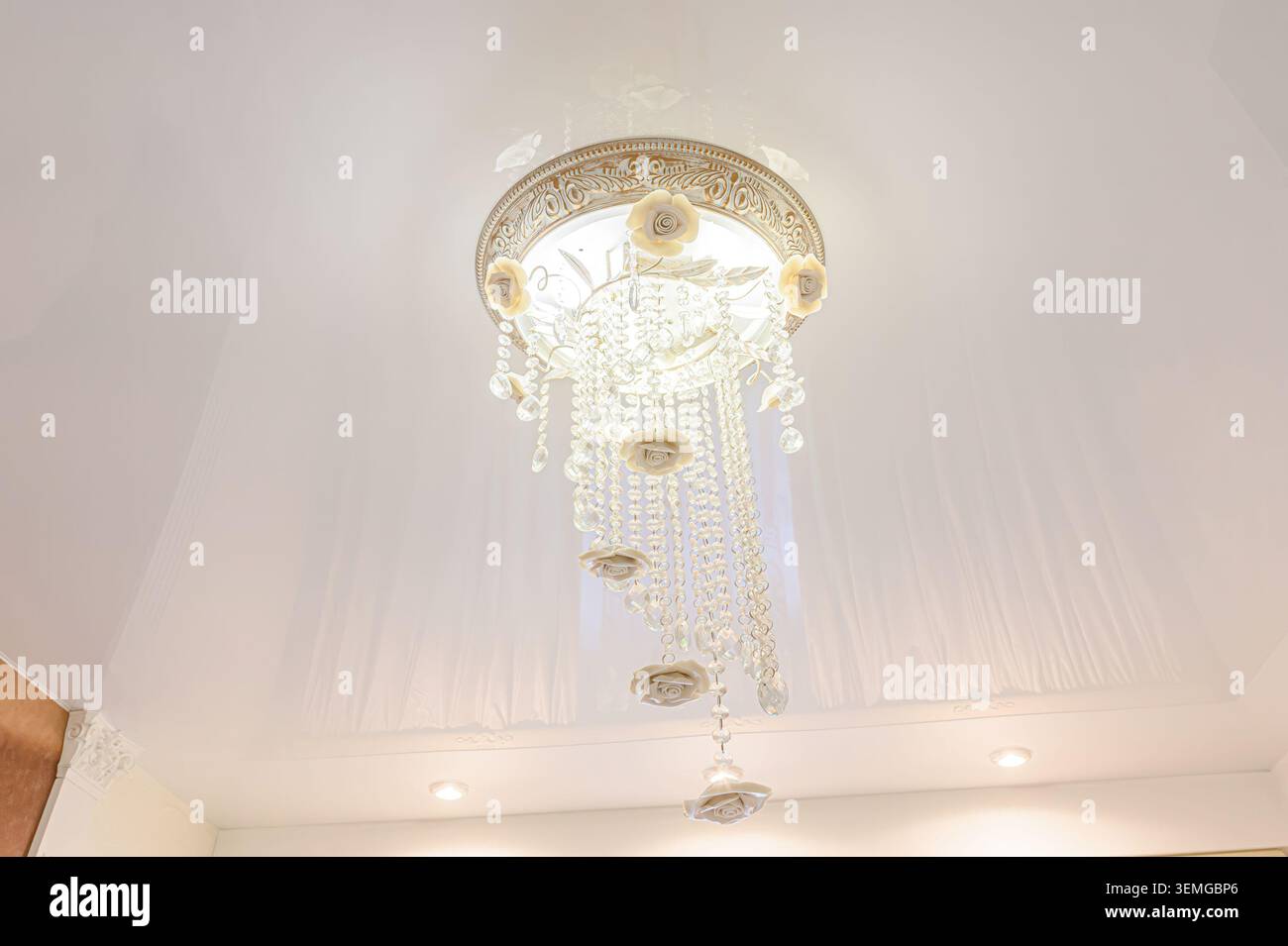 ripresa ad angolo basso di un lampadario decorato appeso a un soffitto bianco. L'apparecchio presenta cristalli, dettagli floreali e una base rotonda decorativa Foto Stock