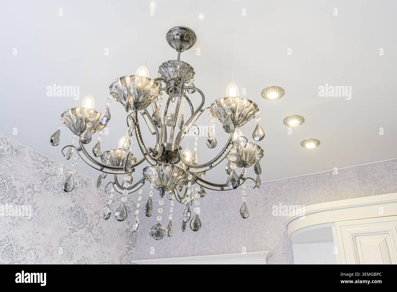 foto dettagliata di un elegante lampadario con lampade a sospensione in cristallo su un soffitto bianco con luci da incasso. Foto Stock