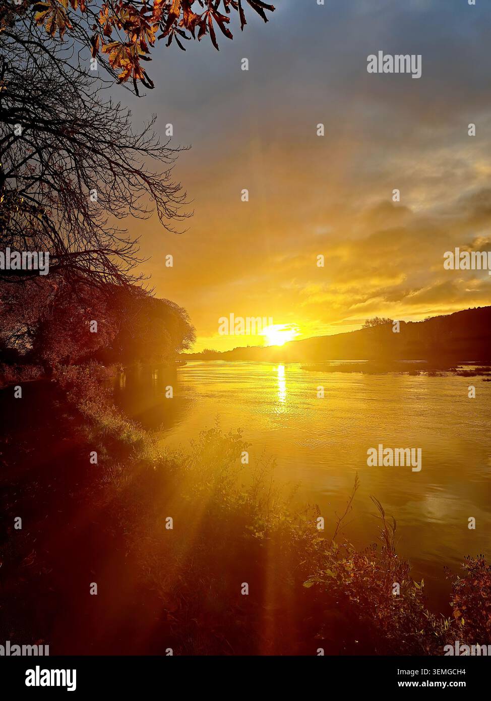 Fasci visibili di un sole che sorge sopra le lontane hils e un ampio fiume. Contea di Tipperary, irlanda. - Immagine stock catturata con smartphone