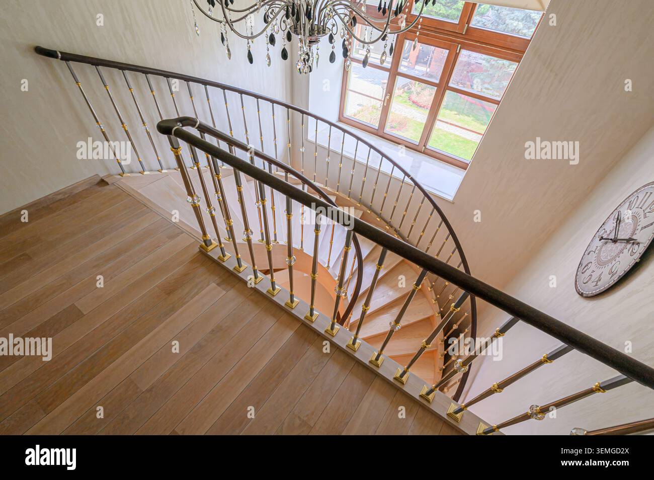 Elegante scala con gradini in legno, corrimano scuro e intricate ringhiere in metallo. Un lampadario è appeso sopra e una finestra offre una vista. Foto Stock