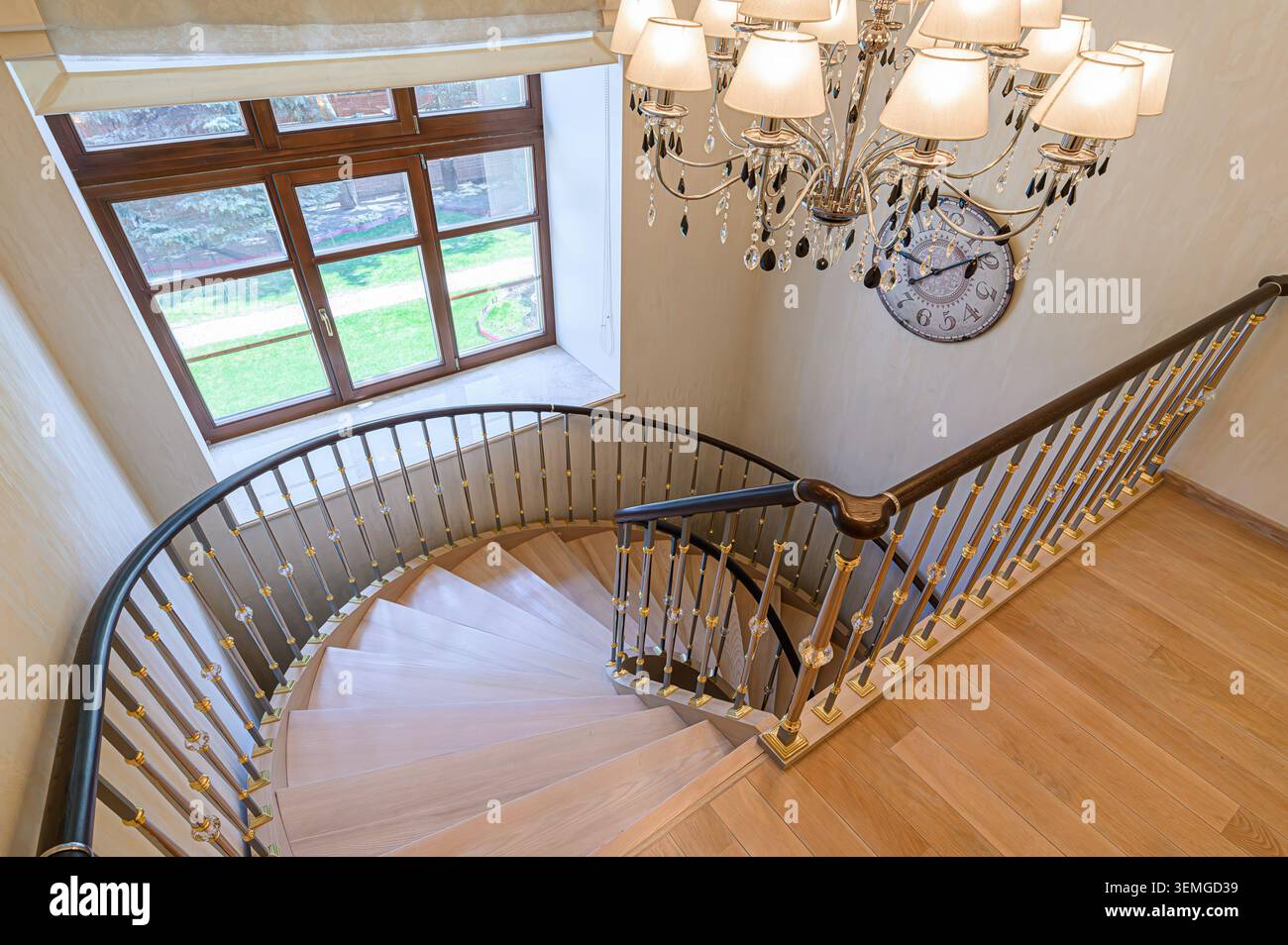 Interni eleganti che presentano una scala a chiocciola, un lampadario e una finestra che si affaccia su un giardino. Foto Stock