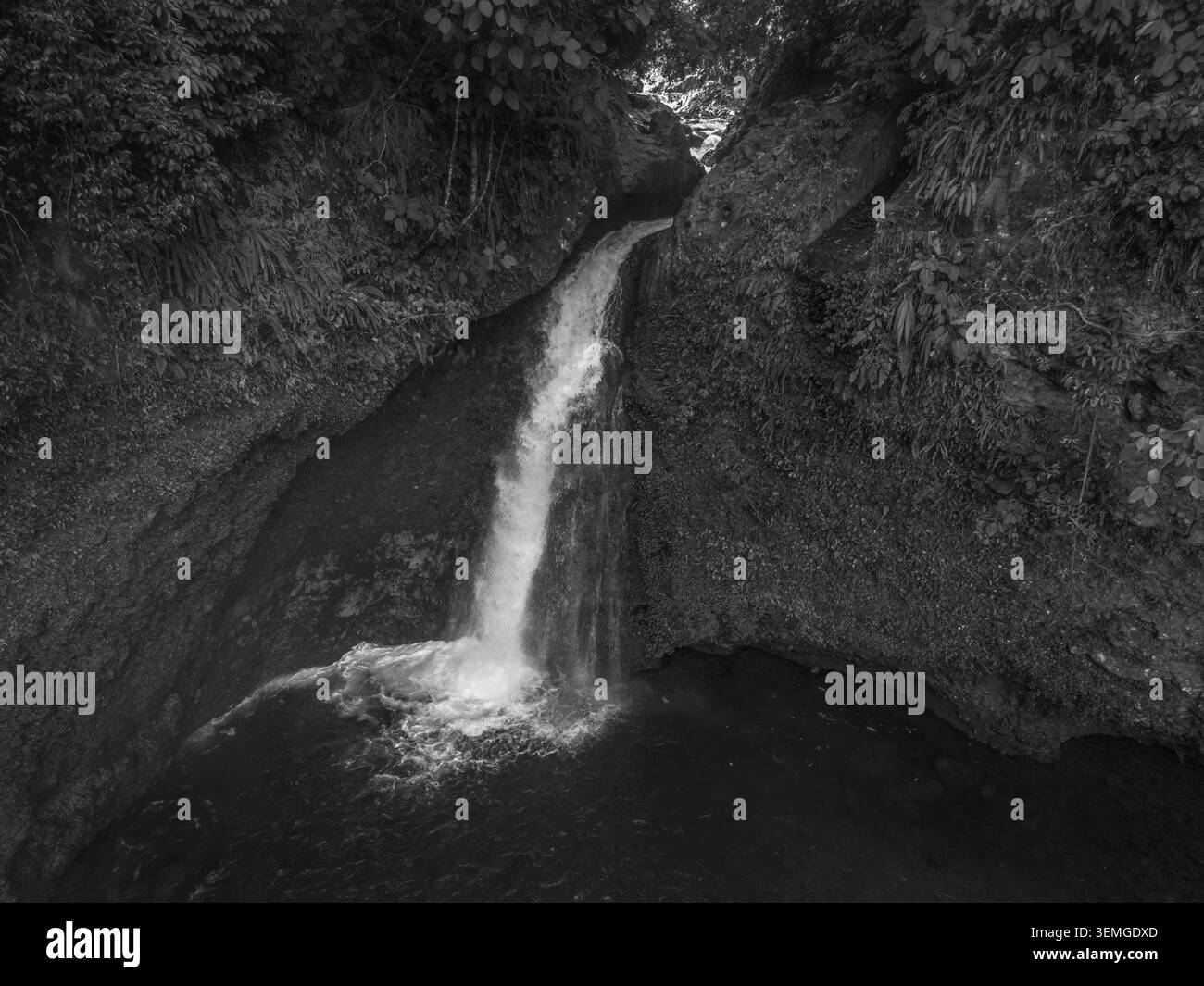Vista aerea di una cascata nascosta nel profondo della lussureggiante foresta pluviale tropicale del Monte Daun, Indonesia. Circondato da una fitta vegetazione verde della giungla, il Foto Stock