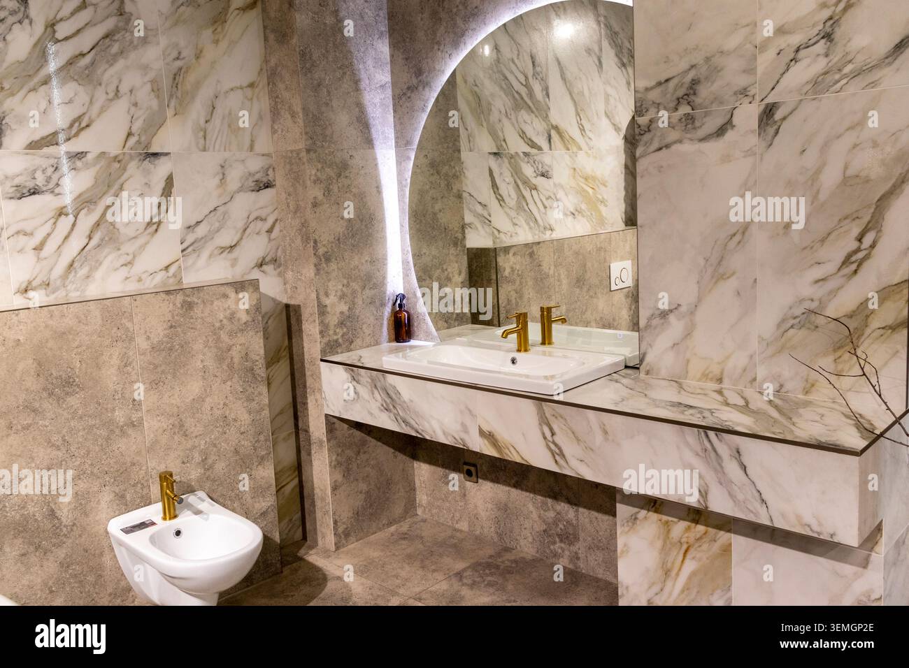 Lussuoso lavandino in marmo con specchio circolare retroilluminato e rubinetto dorato Foto Stock
