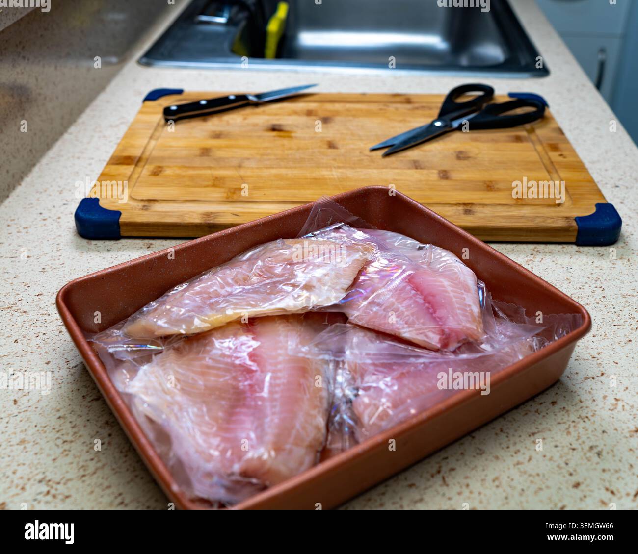 Filetti di pesce crudi in vassoio marrone accanto al tagliere di legno, preparazione di pesce per cucina casalinga per una cucina sana, cena, preparazione dei pasti e concetti alimentari. Foto Stock
