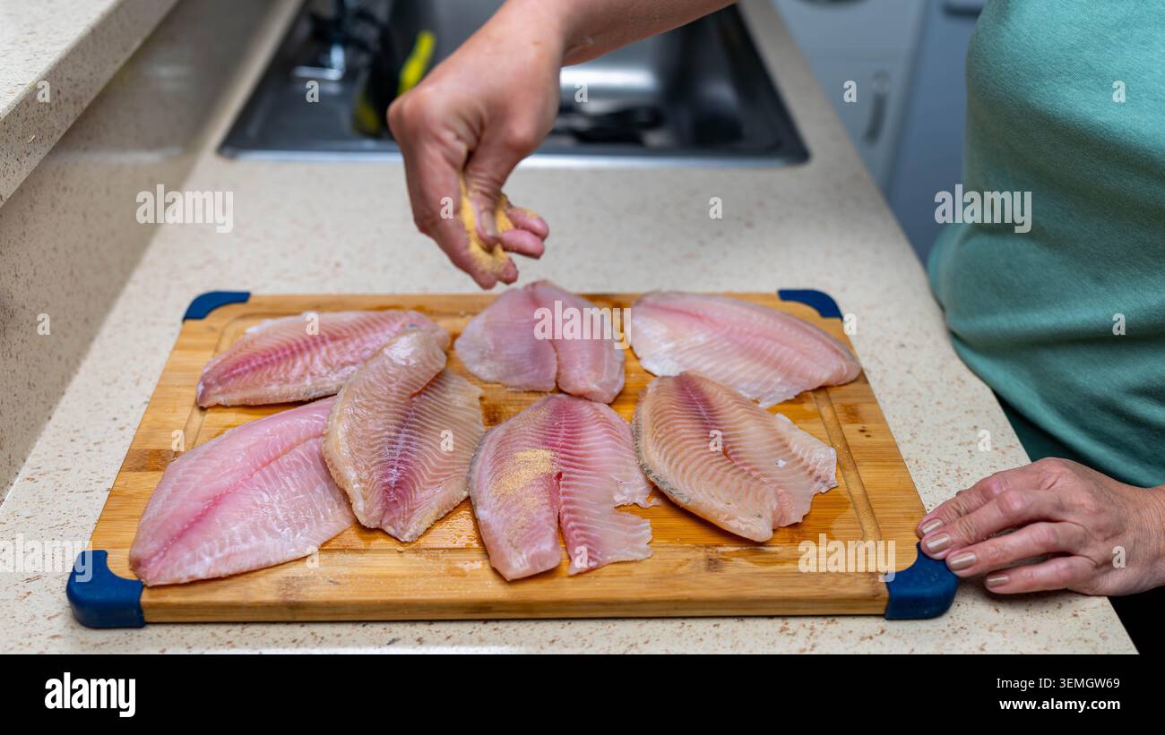 Filetti di pesce tilapia crudi freschi su tagliere in legno nella cucina casalinga, preparazione di pesce per una cucina sana, cena, dieta e concetti alimentari oggi. Foto Stock