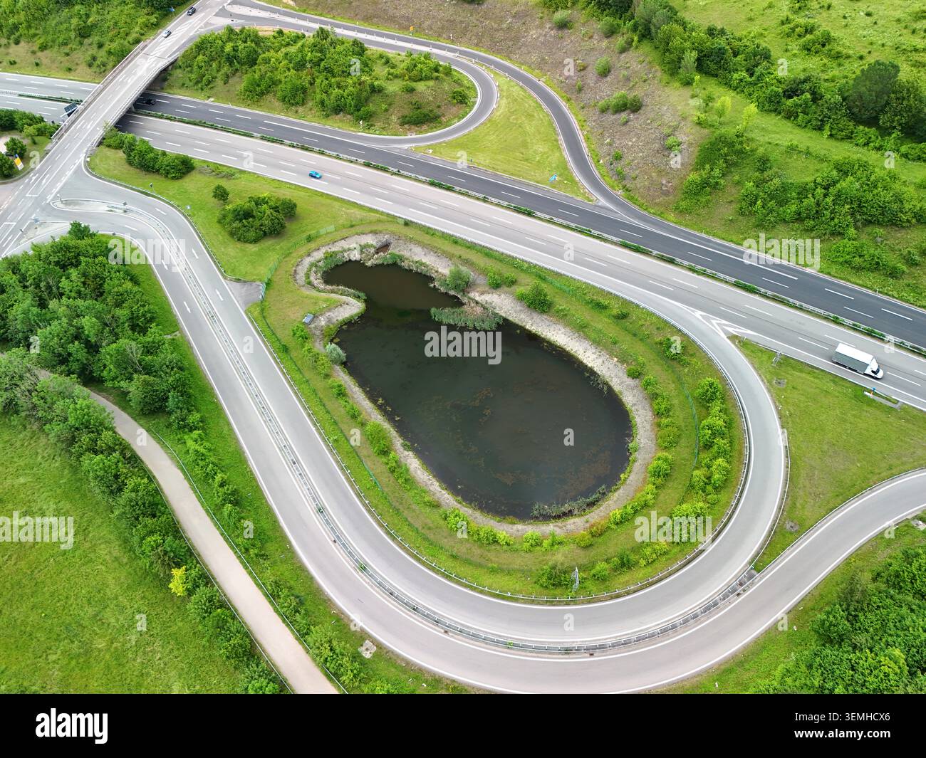 Veduta aerea dello svincolo autostradale con strade curve e laghetto nel paesaggio verde Foto Stock