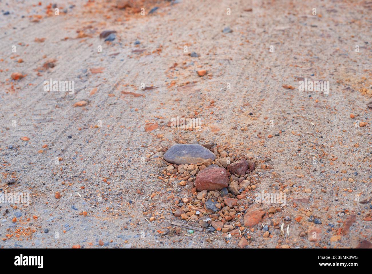 Piccole pietre e frammenti di argilla arancione si trovano sparsi su una superficie stradale sabbiosa asciutta. Vista su un terreno sterrato con pneumatici dalle consistenze sabbiose Foto Stock