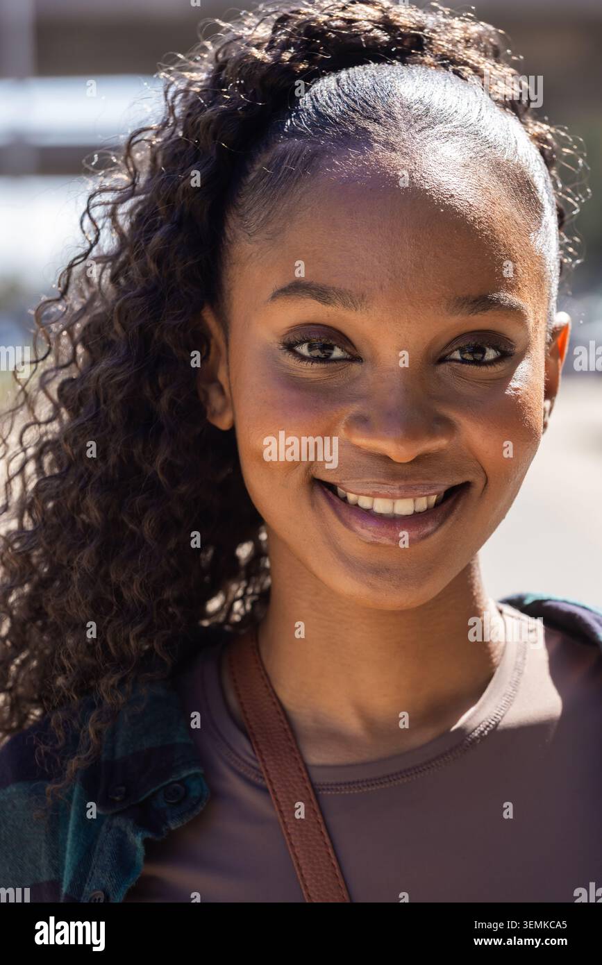Donna afroamericana sorridente guardando la camma all'esterno con indosso una camicia a quadri verde con cinturino marrone Foto Stock