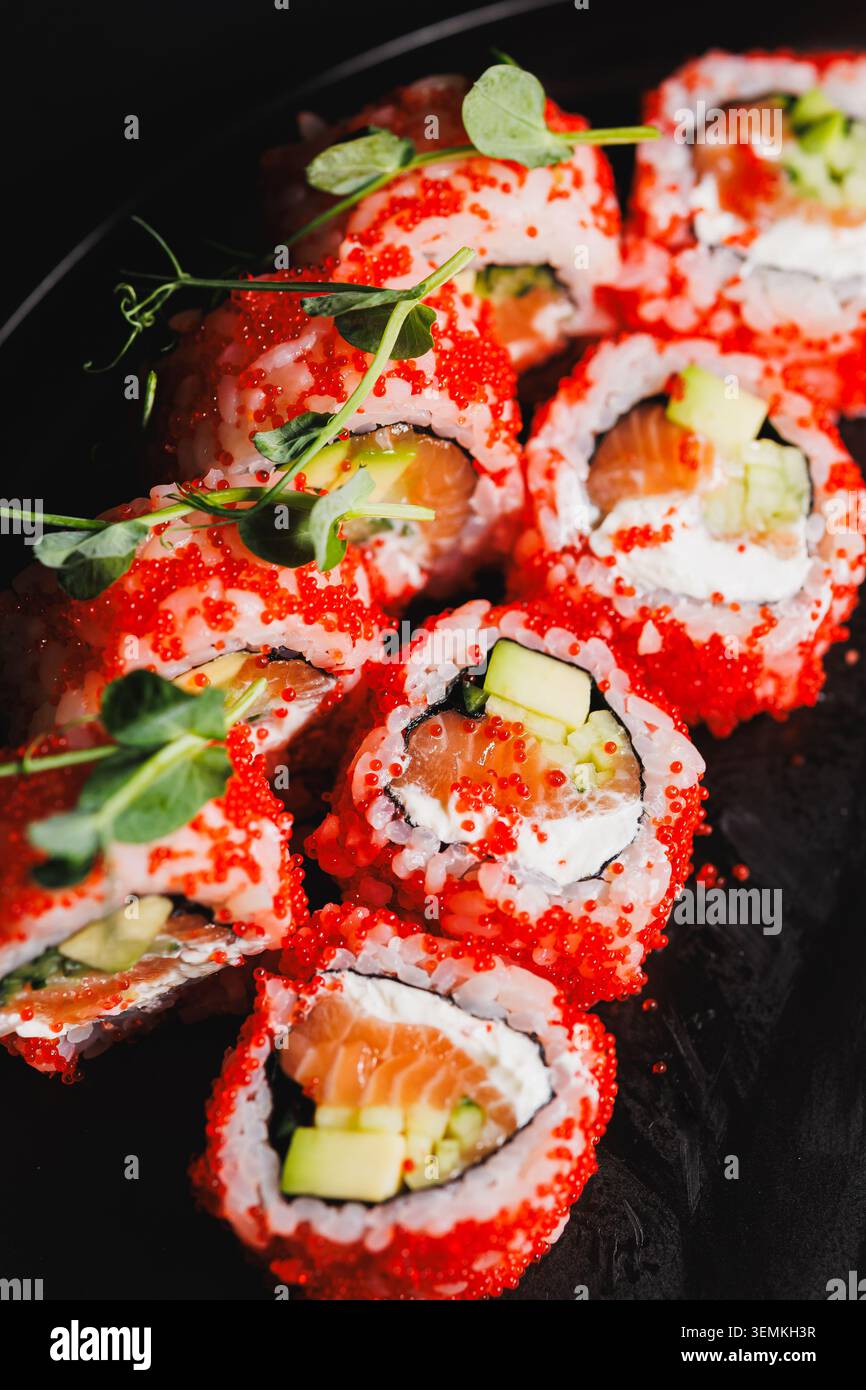 Gli involtini di sushi ripieni di salmone e cetriolo sono disposti su un piatto nero. Sopra i panini c'è un capriolo di pesce rosso brillante. Questo piatto è servito in un restau Foto Stock