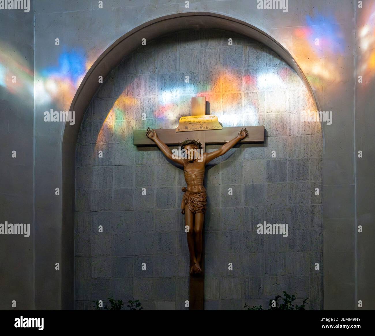 Statua del Crocifisso nella nicchia della chiesa con luce colorata da vetro colorato Foto Stock