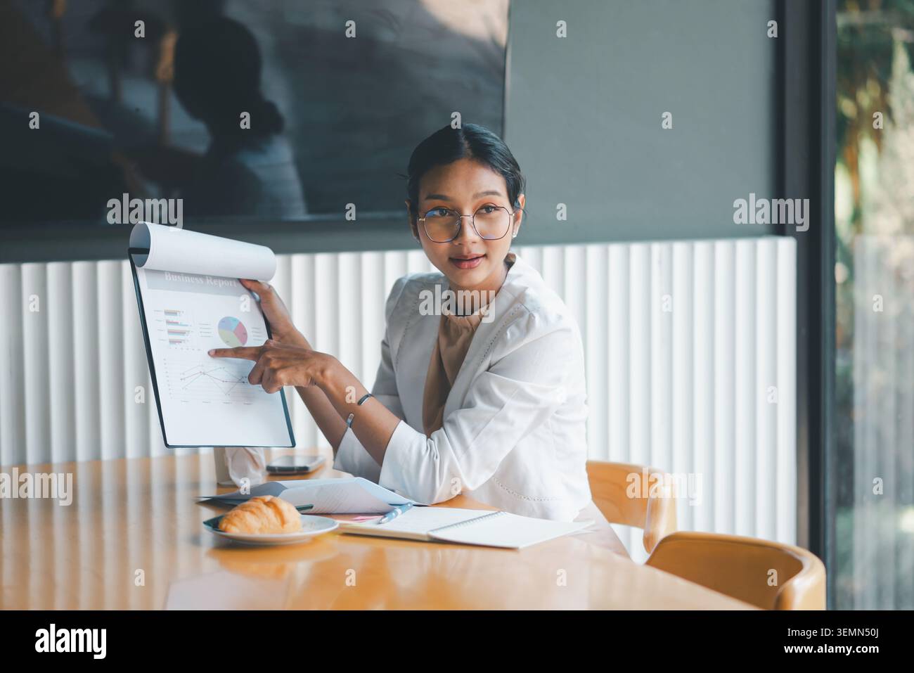 Donna d'affari che indica un report aziendale sugli appunti durante la riunione d'ufficio, spiega i dati grafici, l'analisi di mercato e le metriche delle prestazioni in una modalità Foto Stock