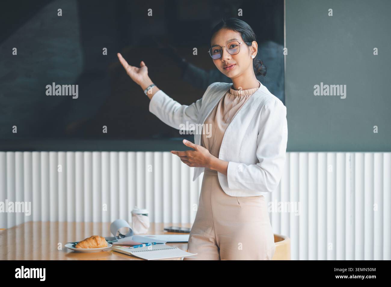 Donna d'affari in piedi accanto a uno schermo di presentazione vuoto in un ufficio moderno, che utilizza i gesti delle mani per introdurre idee, spiegare la strategia e fornire copia Foto Stock