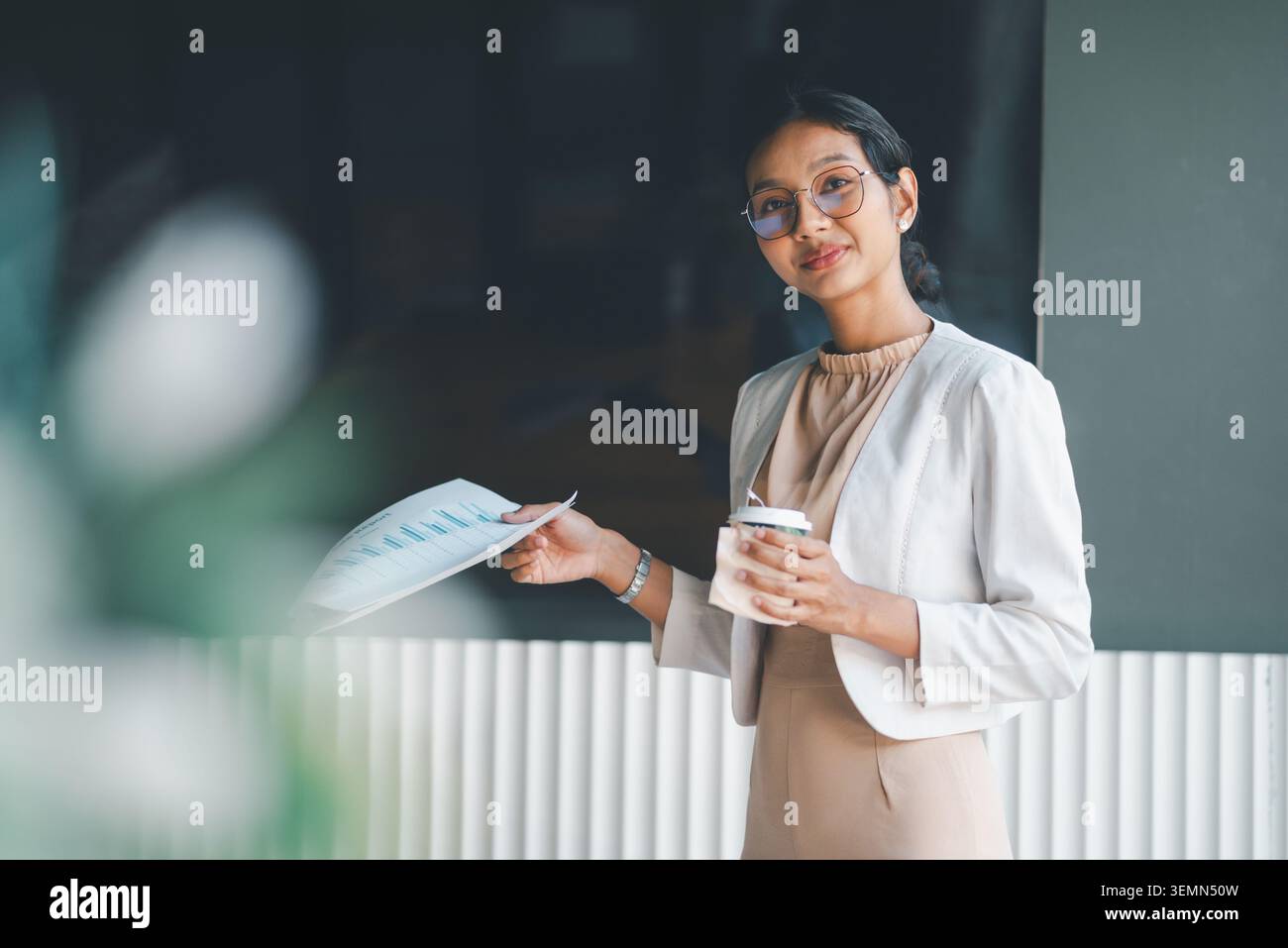 Donna d'affari sicura che tiene un rapporto e una tazza di caffè in ufficio, si ferma durante una presentazione con postura professionale tranquilla, documenti aziendali e. Foto Stock