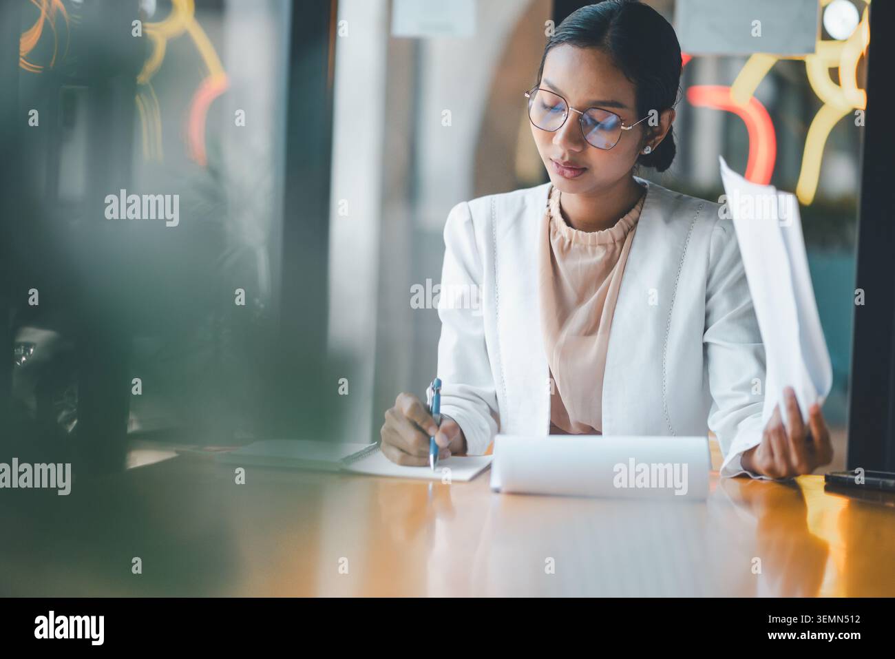 Donna d'affari concentrata che scrive appunti e tiene i documenti alla scrivania, esamina i documenti, pianifica le attività e organizza le informazioni durante un periodo di calma Foto Stock