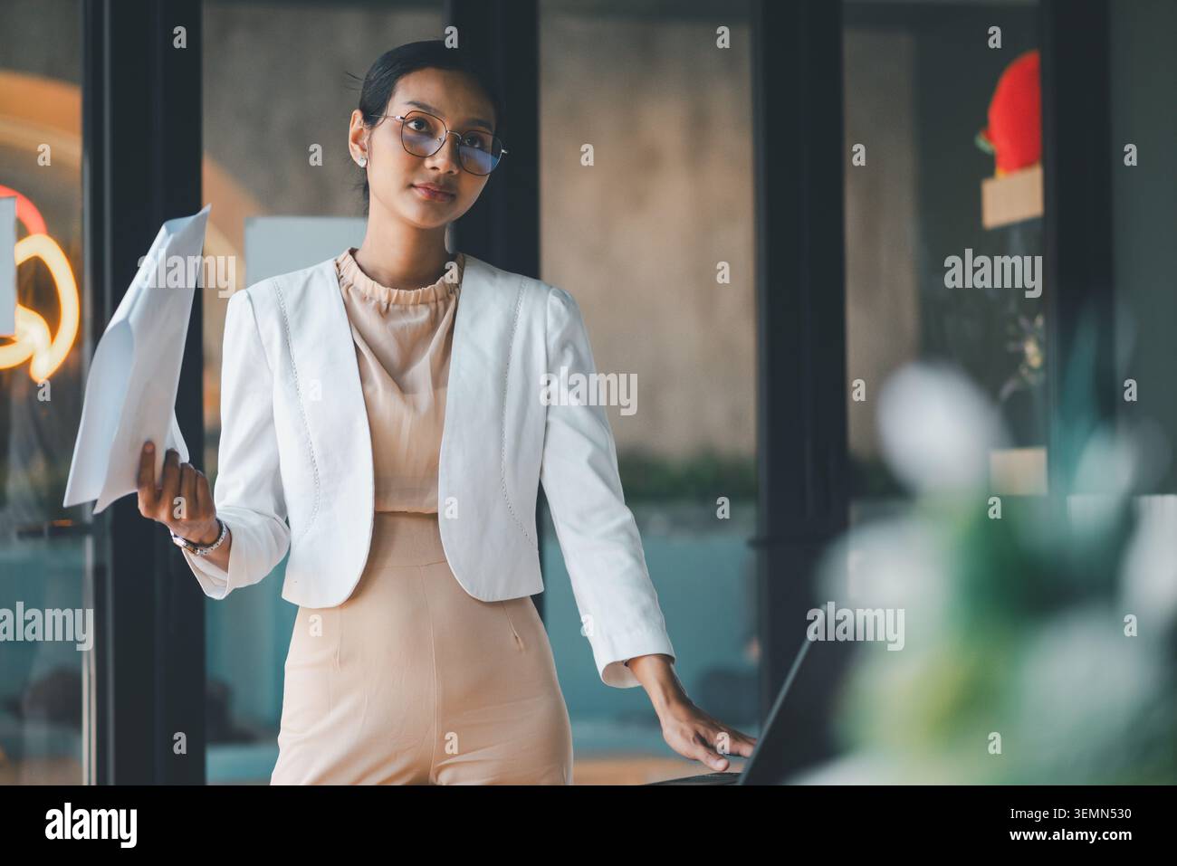 Donna d'affari seria in piedi con i documenti accanto al laptop durante una riunione d'ufficio, preparandosi a spiegare la strategia di progetto, l'analisi aziendale e la professione Foto Stock
