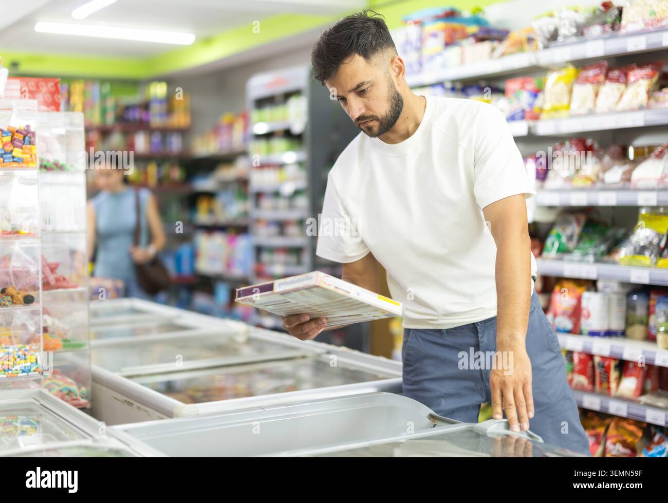 Uomo adulto in piedi presso il frigorifero, che sceglie alimenti surgelati nel supermercato. Foto Stock