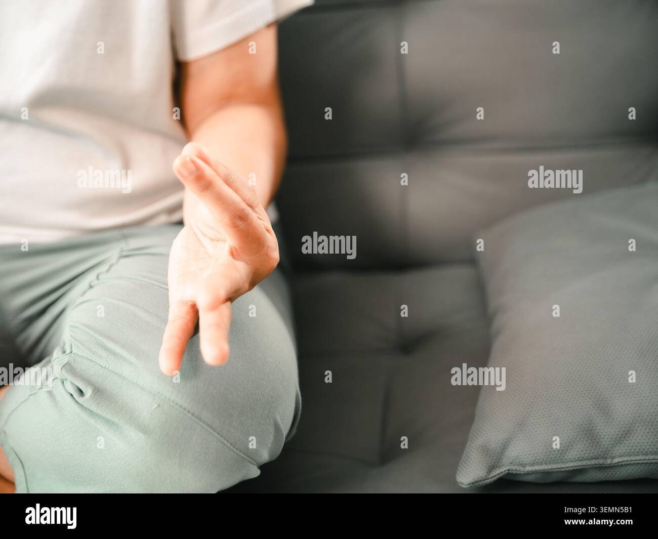 Primo piano di una donna asiatica che pratica un gesto distensivo della mano seduto su un divano a casa, mostrando consapevolezza, meditazione, relax, respirazione, Foto Stock