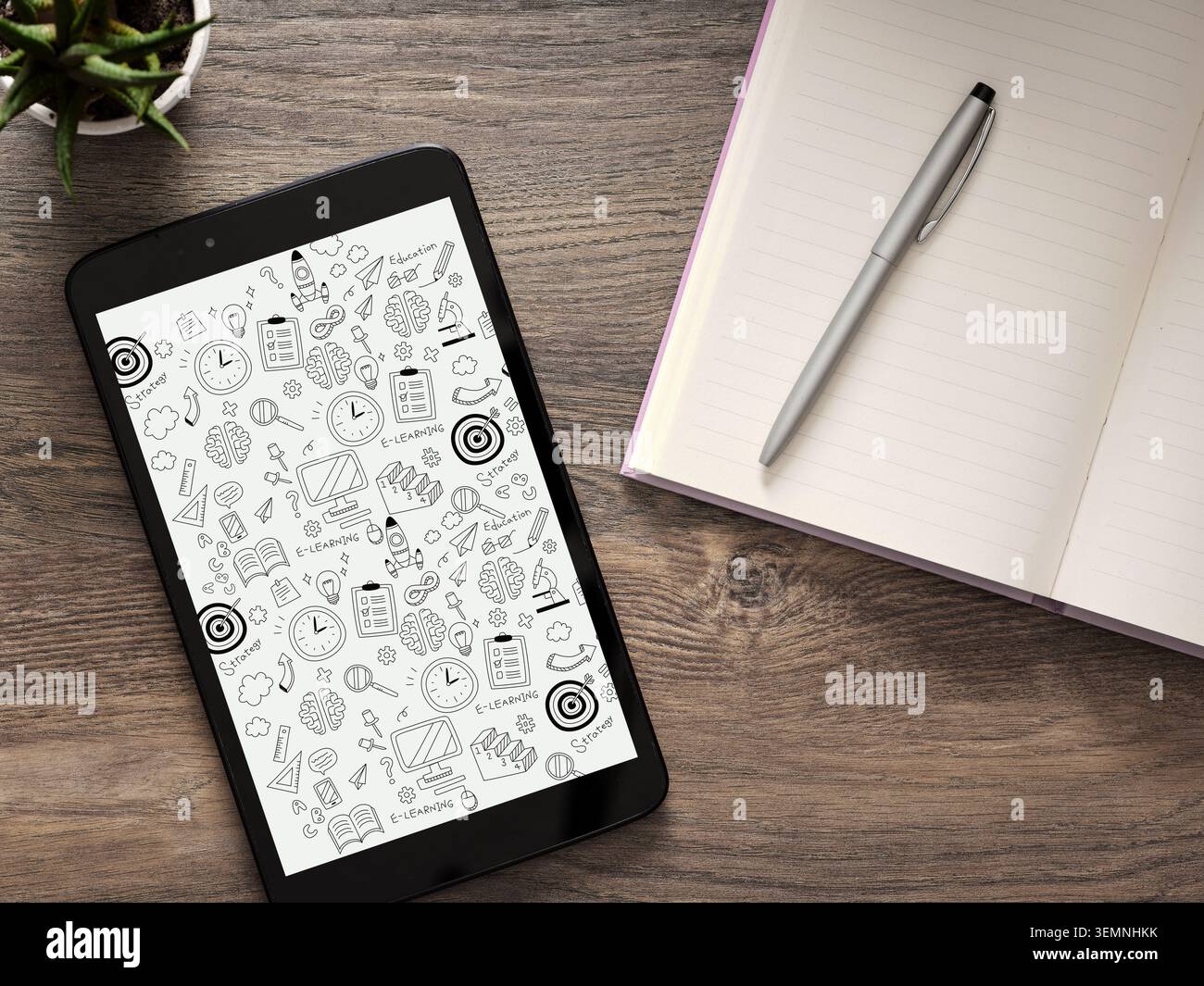 Tablet che mostra vari scarabocchi relativi all'e-learning e all'istruzione, accanto a un notebook aperto e a una penna su una scrivania di legno Foto Stock