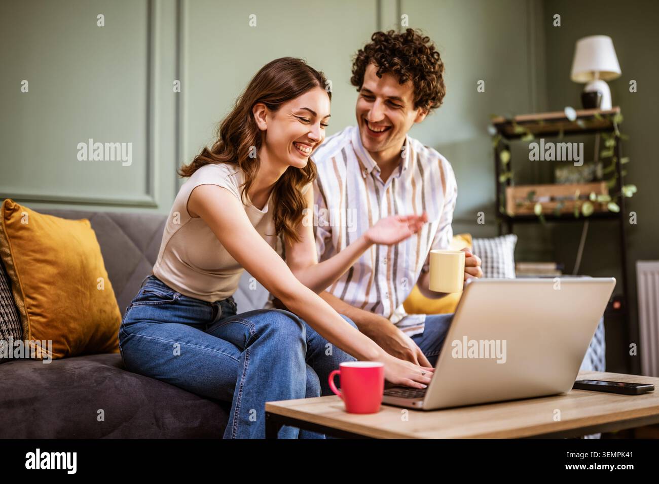 Due giovani adulti si siedono a stretto contatto su un divano, concentrati su un notebook e condividono un momento piacevole. Foto Stock