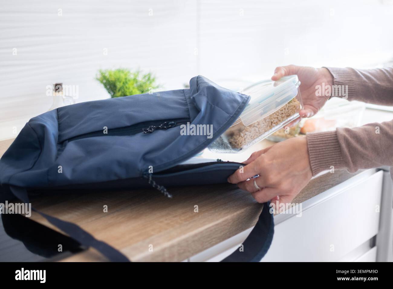 Donna che mette un sano contenitore per pasti fatti in casa in uno zaino. Cibo preparato con verdure, cereali e salmone pronto per essere portato al lavoro, a scuola o fuori Foto Stock
