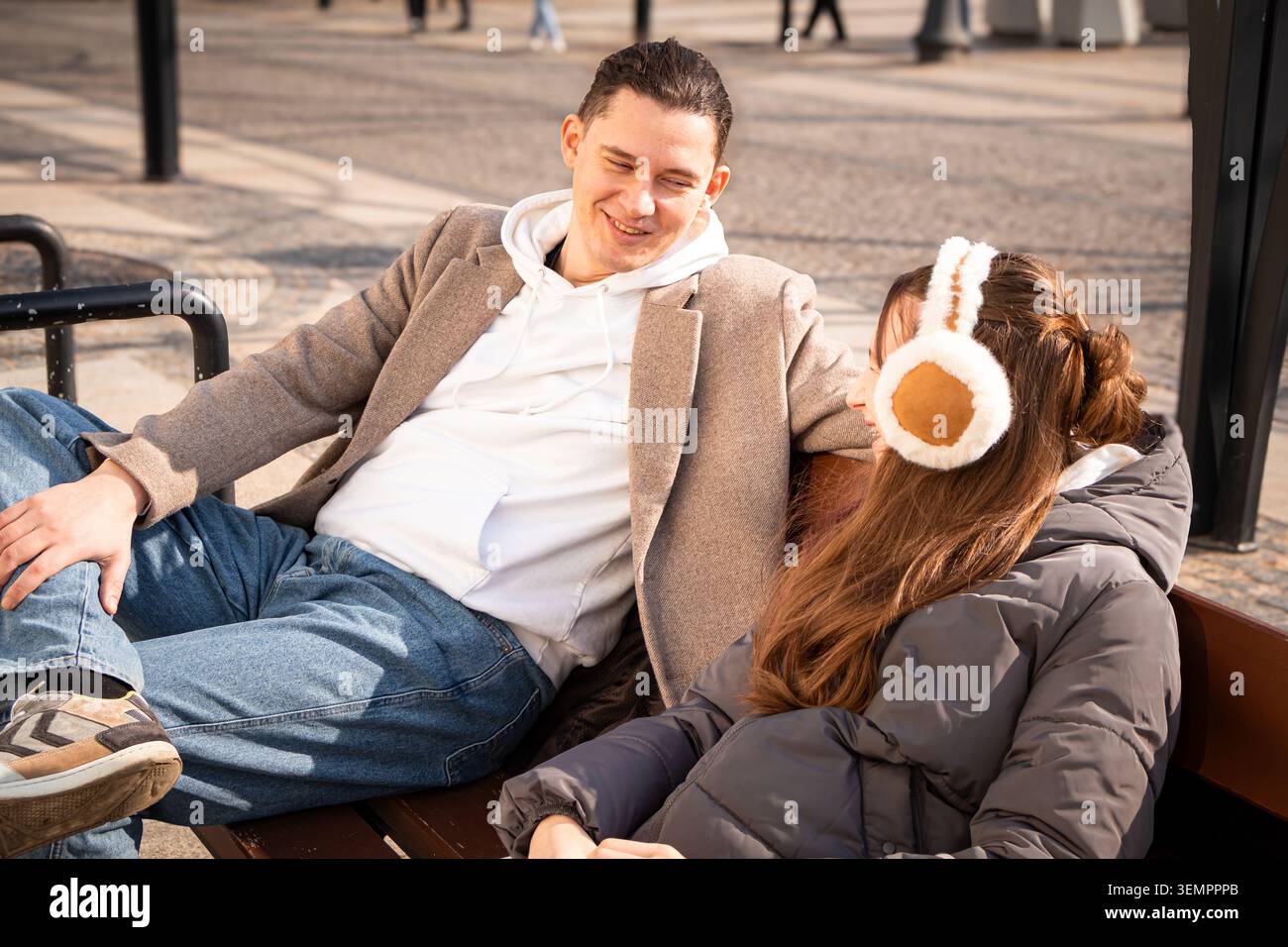 Padre e figlia seduti su una panca intelligente alimentata a energia solare, parlano e trascorrono del tempo insieme mentre ricaricano uno smartphone. Concetto di legame familiare, Foto Stock