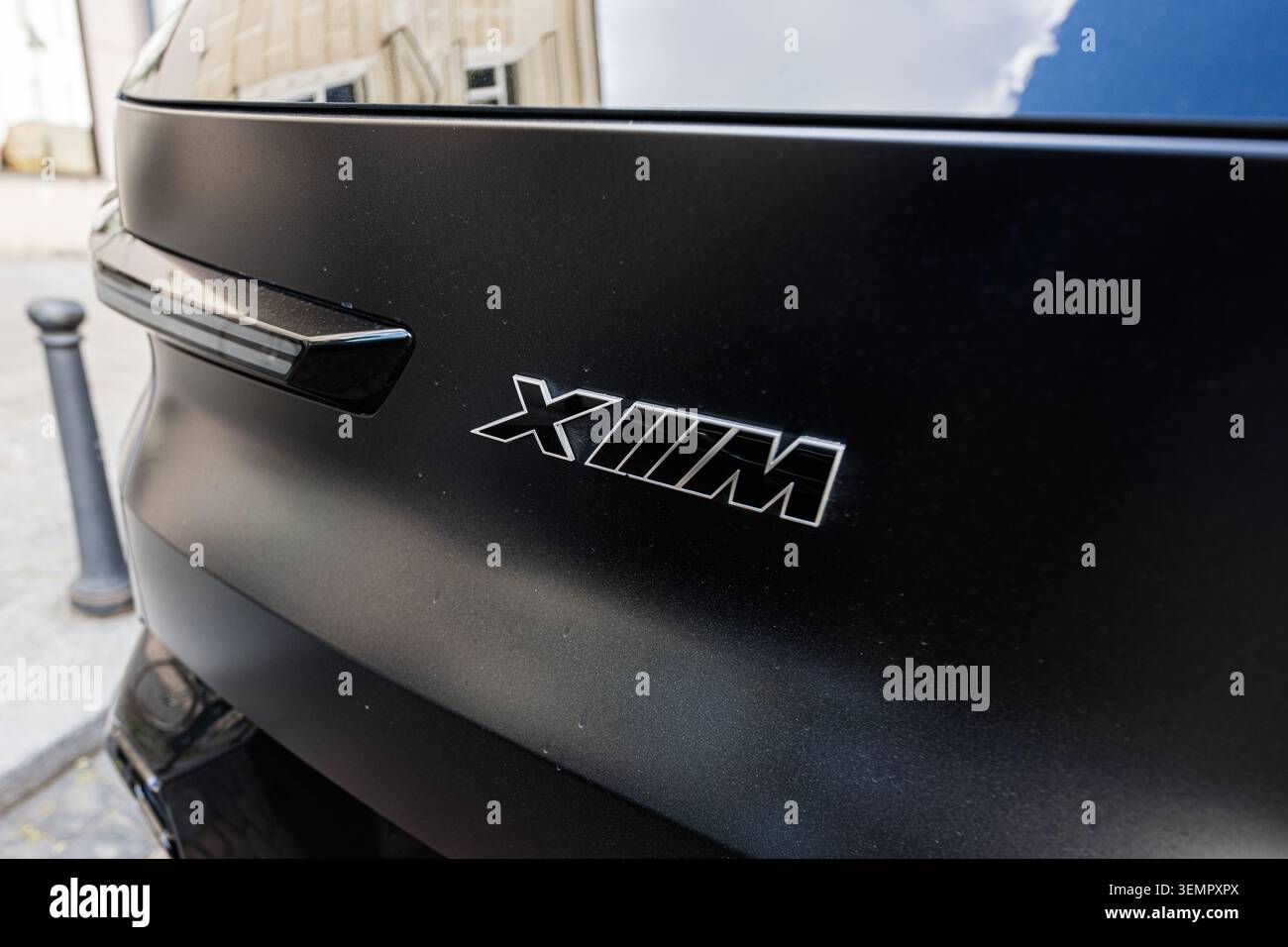 Vilnius, Lituania - 1 giugno 2026: Primo piano di un emblema nero per auto BMW XM sul pannello posteriore che mostra lettere cromate, finitura opaca e riflessi urbani. Foto Stock