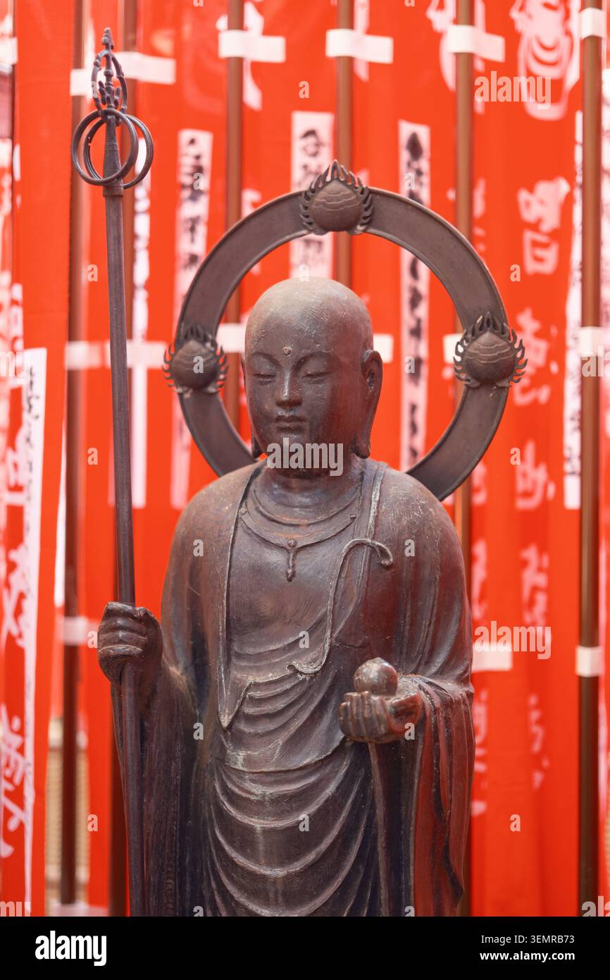 Statua di Buddha in legno posta su un vibrante sfondo di striscioni rosse con testo calligrafico nero, Tokyo, Giappone Foto Stock
