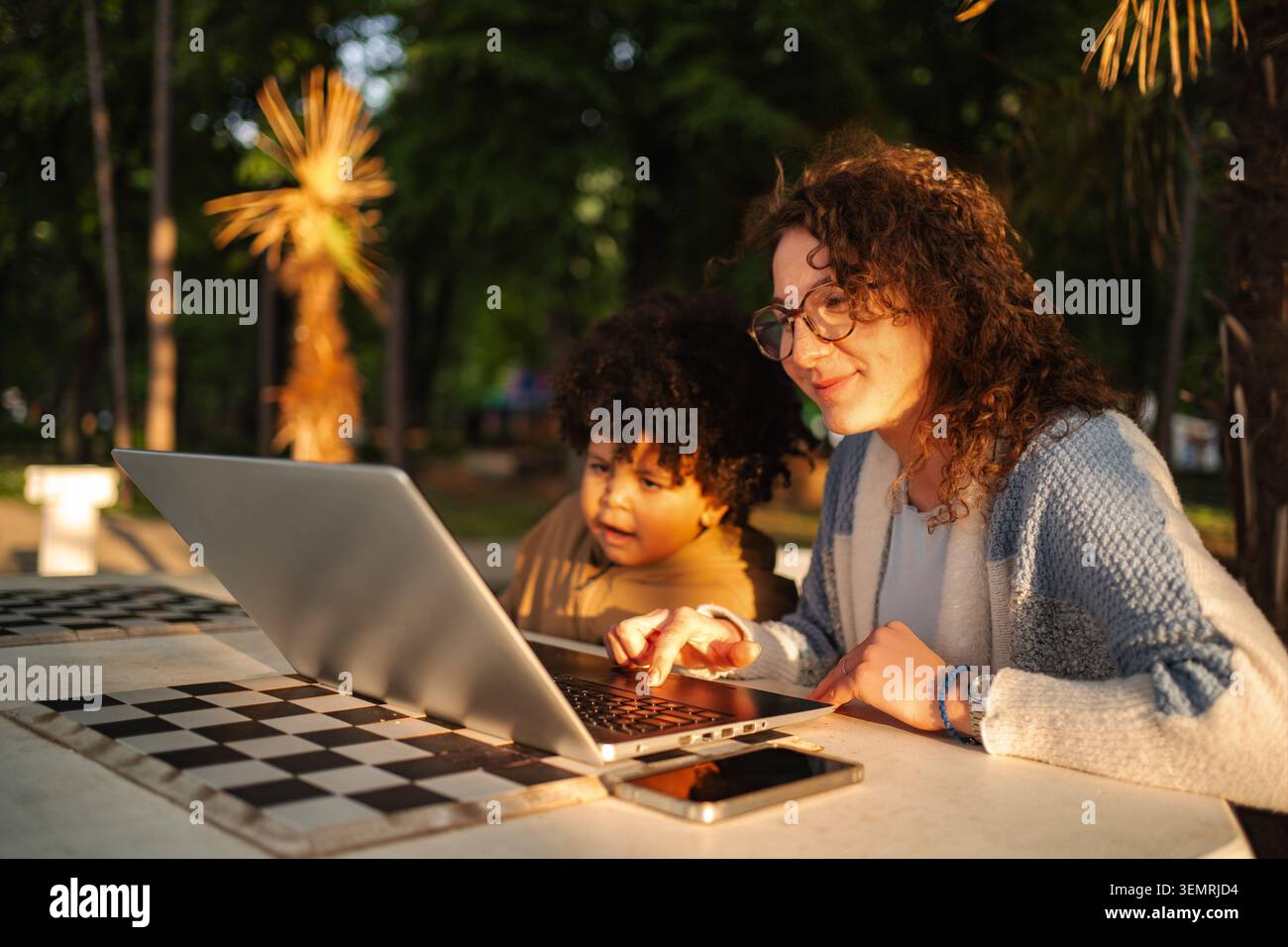 Donna e bambino imparano all'aperto utilizzando un notebook insieme Foto Stock