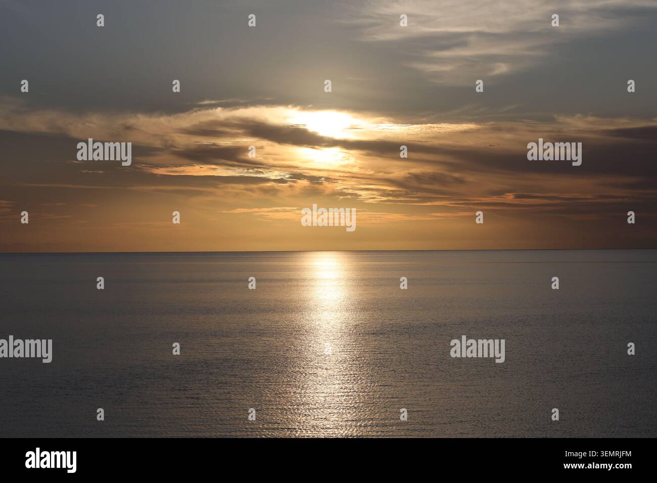 le nuvole brillano di arancione, rame, oro, bianco accecante sopra mari calmi mentre il tramonto si avvicina (primo piano, paesaggio, tropicale) Foto Stock