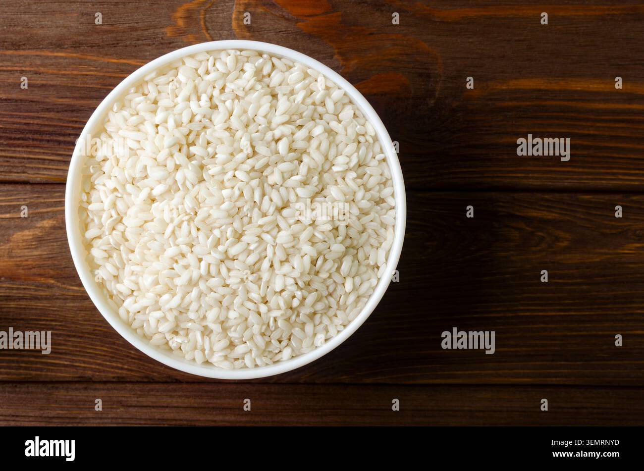 Una ciotola bianca di riso Arborio su una tavola di legno. Concetto di cucina italiana, risotto e alimentazione sana. Riso crudo. Cucina mediterranea. Rus Foto Stock