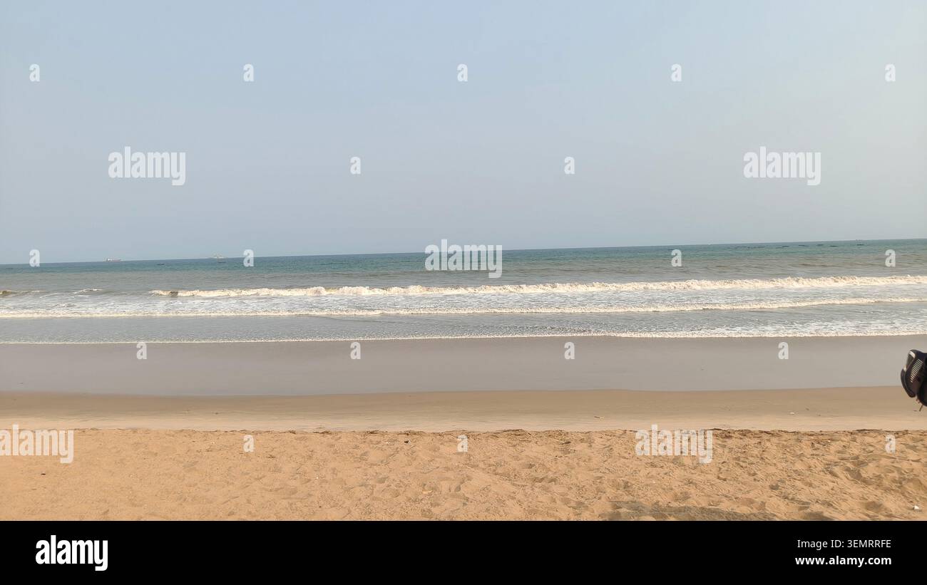 Le tranquille onde oceaniche si infrangono dolcemente su una spiaggia sabbiosa sotto un cielo azzurro limpido, creando un tranquillo paesaggio costiero e un paesaggio marino panoramico. - Immagine stock catturata con smartphone