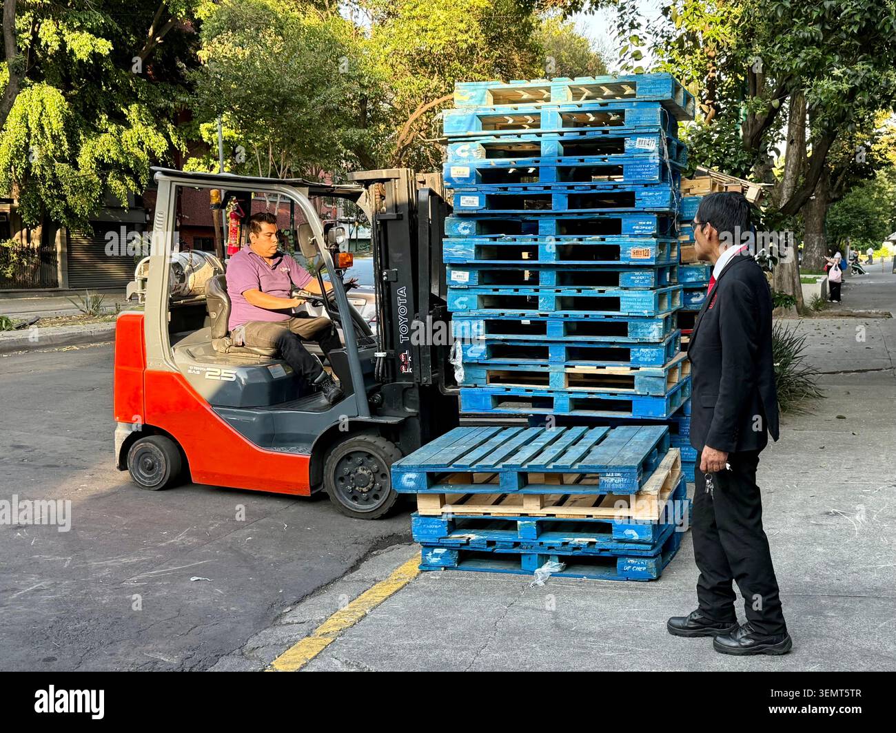 Un carrello elevatore scarica pallet blu impilati all'esterno di un supermercato locale a Roma Norte, città del Messico, Messico. Foto Stock