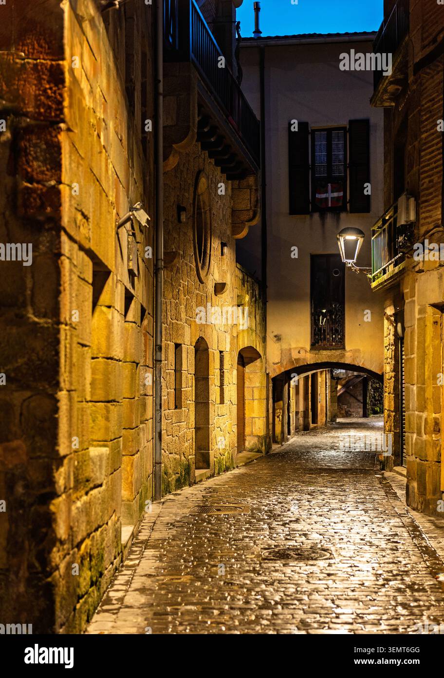 Antico vicolo in pietra (via Donibane) con ciottoli bagnati e lampioni luminosi durante una tranquilla notte invernale a Pasajes de San Juan. Paesi Baschi. Foto Stock