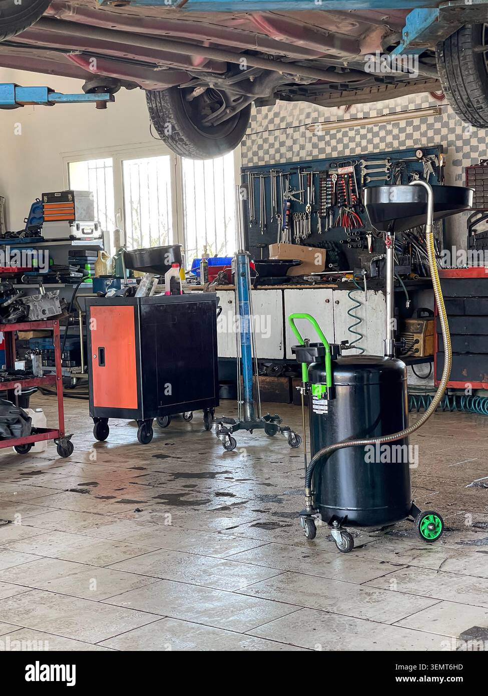 Officina di riparazione auto, manutenzione del veicolo in officina di riparazione auto con attrezzatura di scarico dell'olio sotto la vettura sollevata - Immagine stock catturata con smartphone