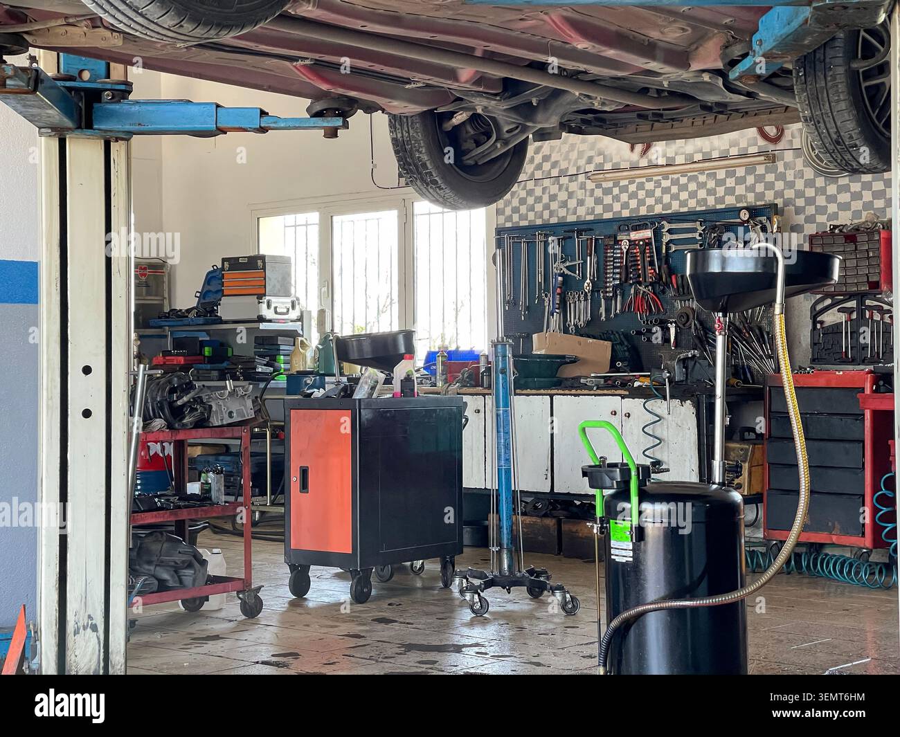 Officina di riparazione auto, manutenzione del veicolo in officina di riparazione auto con attrezzatura di scarico dell'olio sotto la vettura sollevata - Immagine stock catturata con smartphone