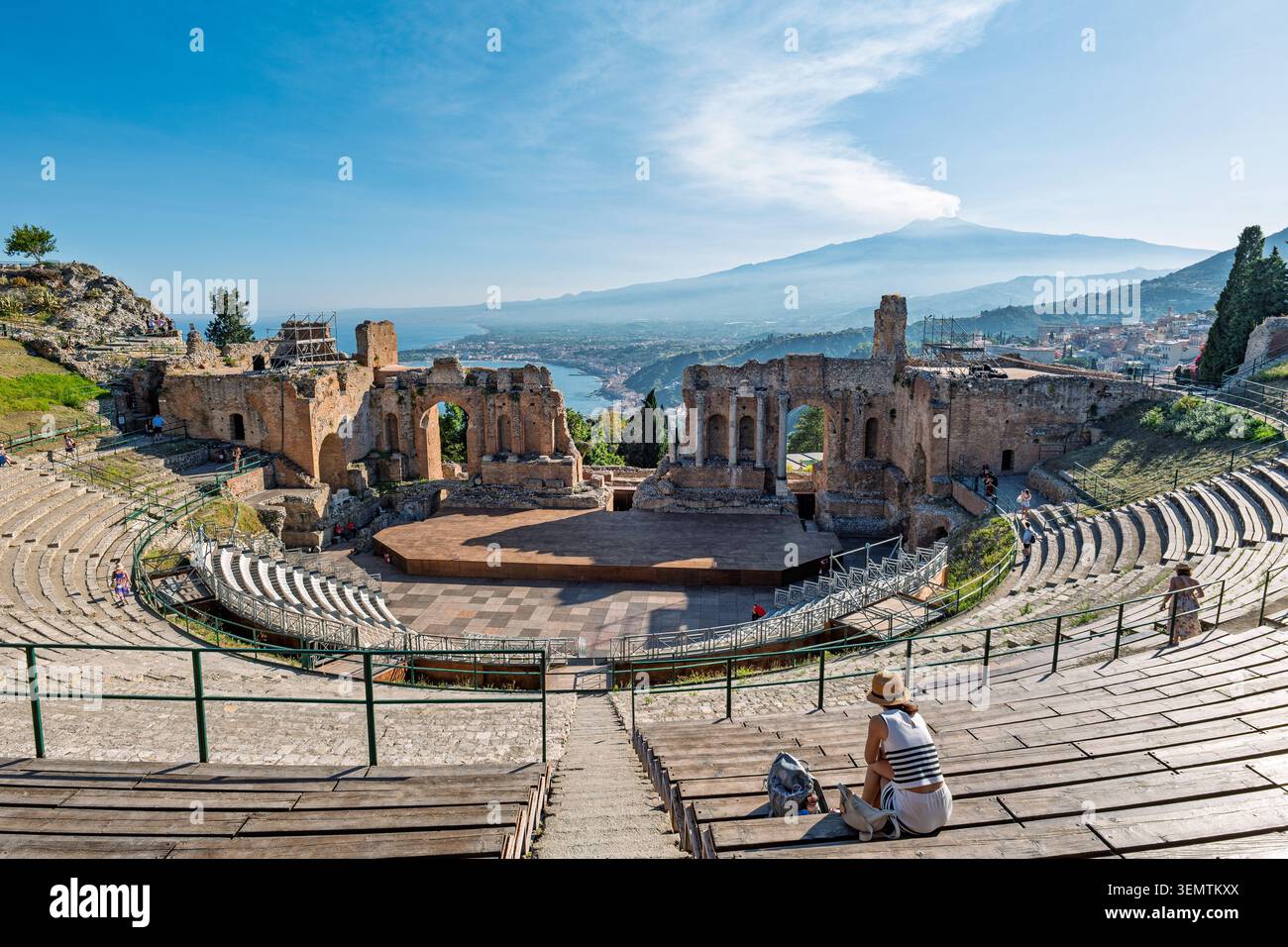 Una donna solitaria siede sui sedili in pietra intemprata dell'antico Teatro Greco di Taormina, guardando le rovine semicircolari verso il dra Foto Stock