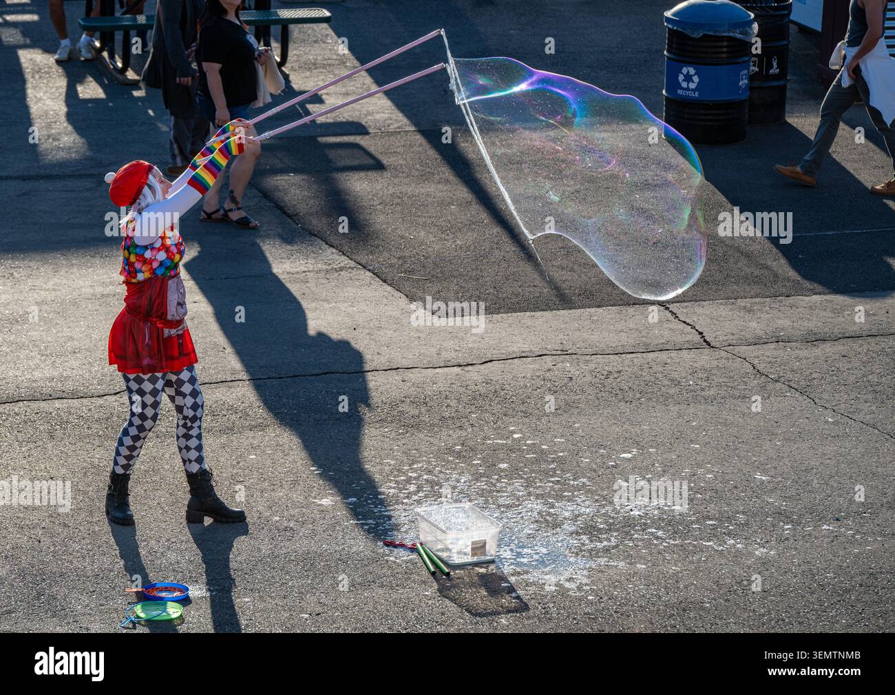 Un colorato artista di strada crea una bolla gigantesca e iridescente durante il mese di Pride prima di una partita di calcio. Foto Stock